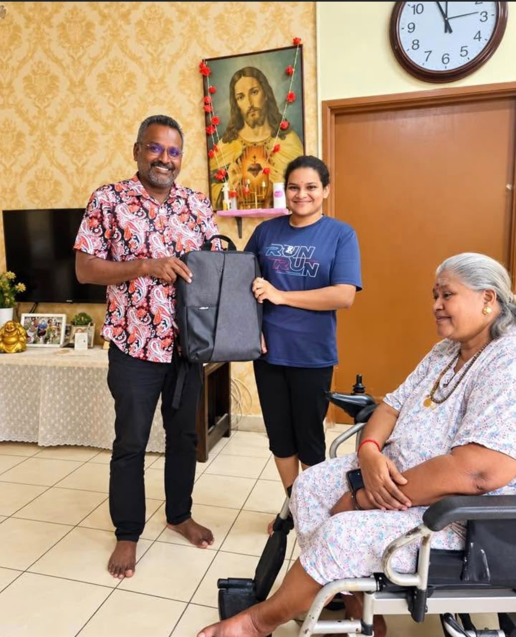 A man and a young woman presenting a laptop backpack to a woman seated in a wheelchair