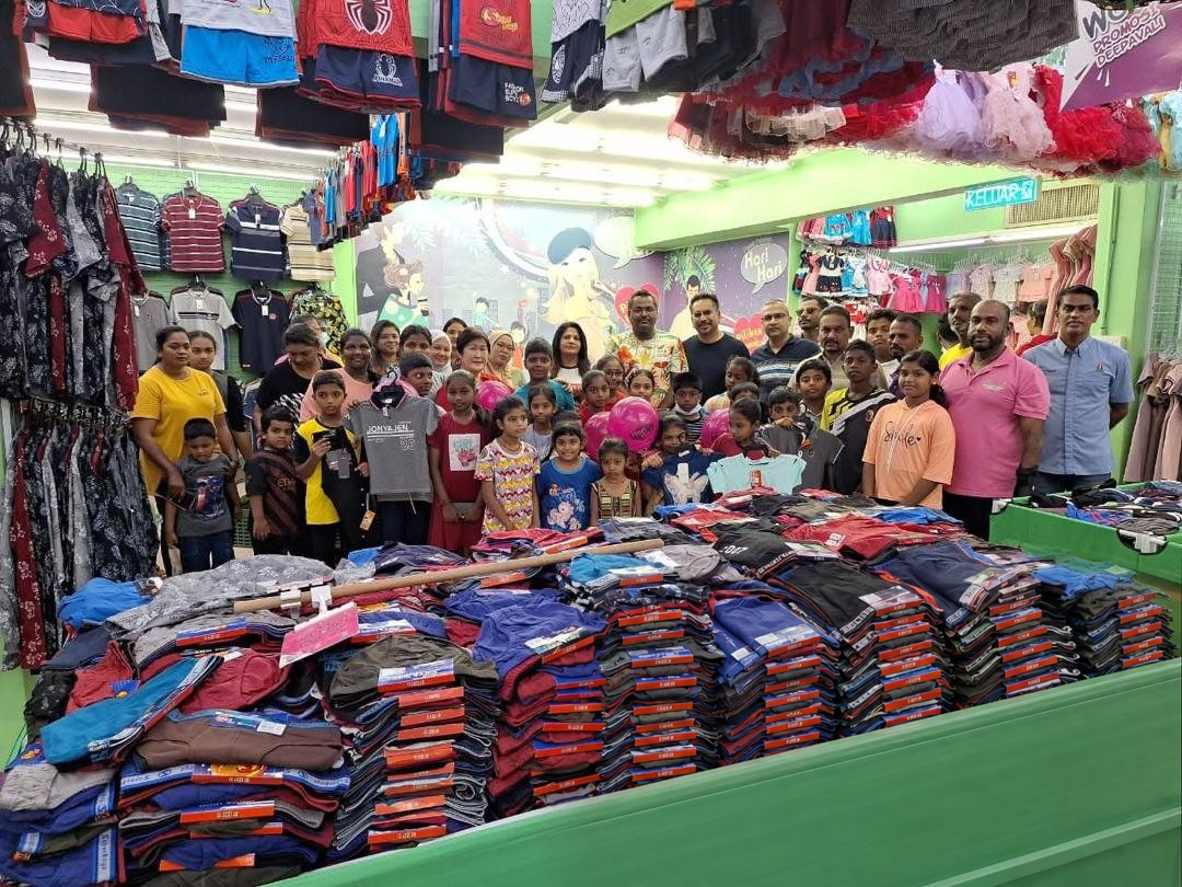 A large group of children and adults standing behind a table stacked with new clothing